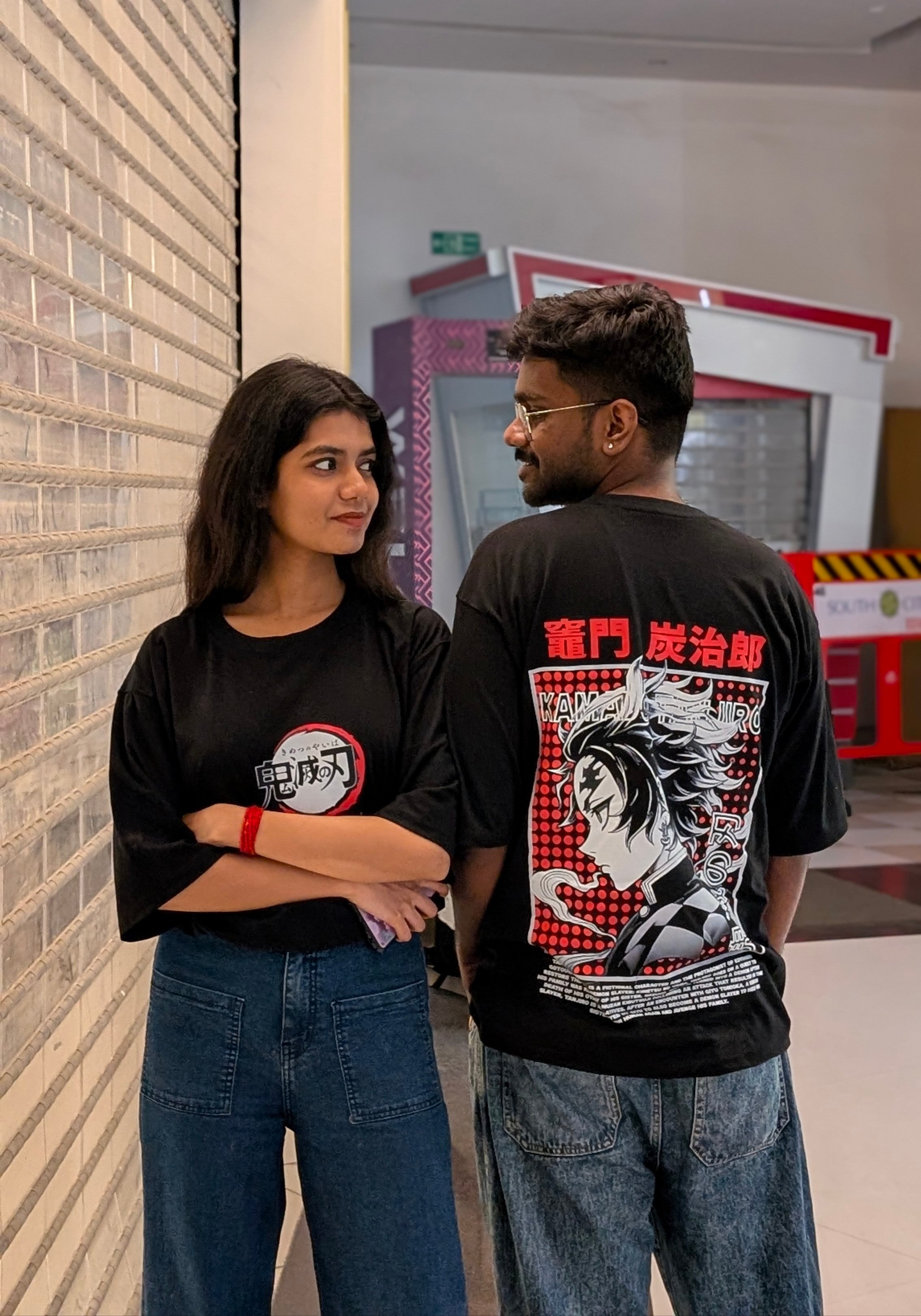 Two people wearing black t-shirts with graphic designs, standing indoors.